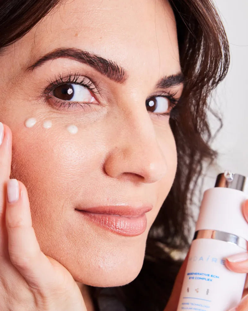 Close-up of woman applying white cream near eye holding Triple Threat 