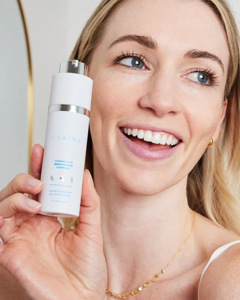 Smiling woman holding Vitamin C-FK  Brightening Complex bottle close t