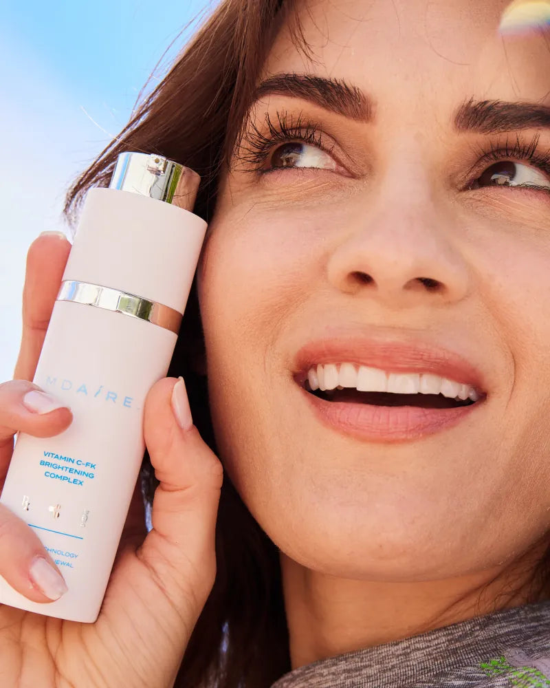 Woman smiling and holding Vitamin C-FK  Brightening Complex bottle clo