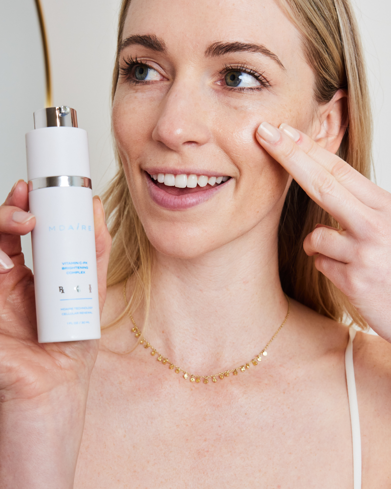Smiling woman showing application of Vitamin C-FK  Brightening Complex on cheek in gallery position 1